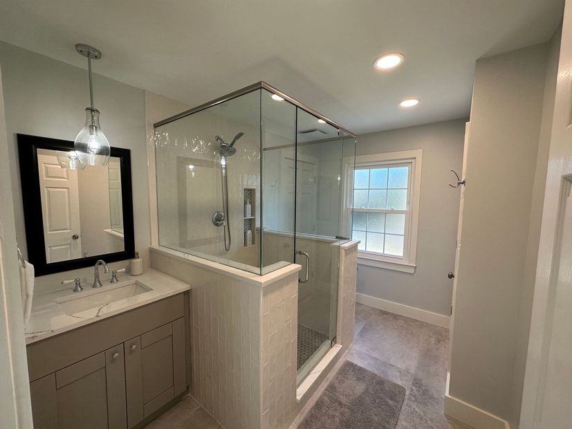 A bathroom with a walk in shower , sink , mirror and window.