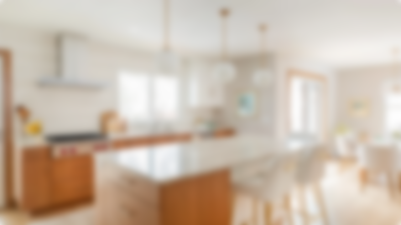 Bright, blurred open kitchen and dining area with wooden furniture and white countertops