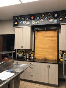 Kitchen with light wood cabinets, black countertop, and a window with a bamboo blind and decorative wall plates above.