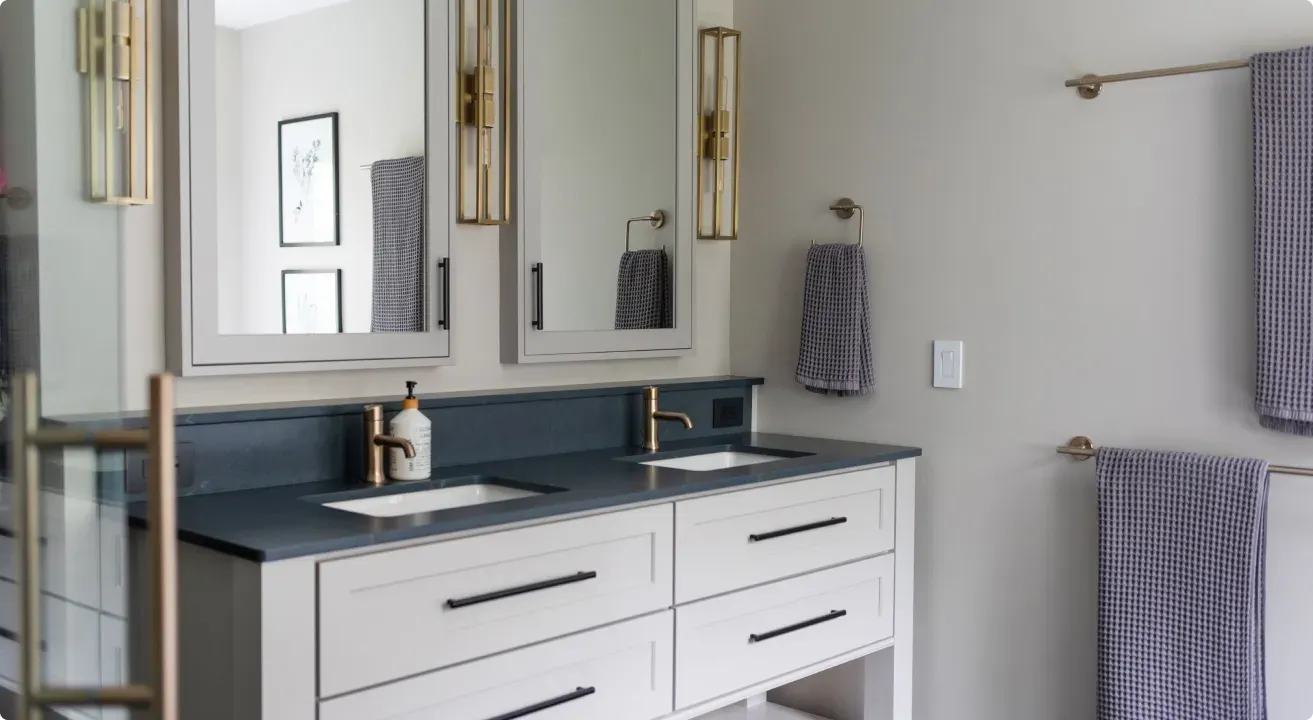 Modern bathroom vanity with double mirrors, white cabinets, blue countertop, and hanging towels