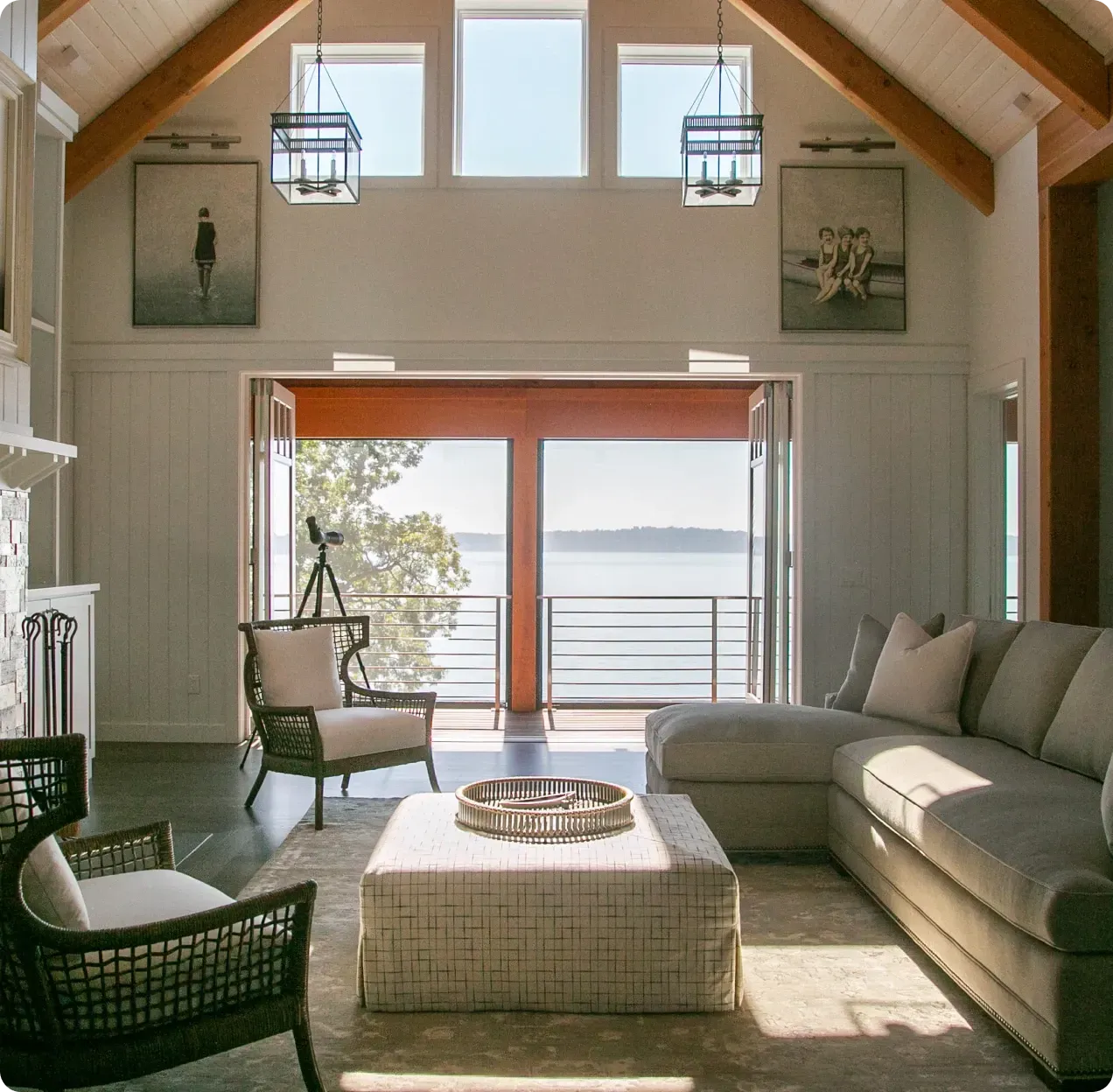 Bright living room with vaulted ceiling, large windows, sofa, chairs, and an ocean view through open doors