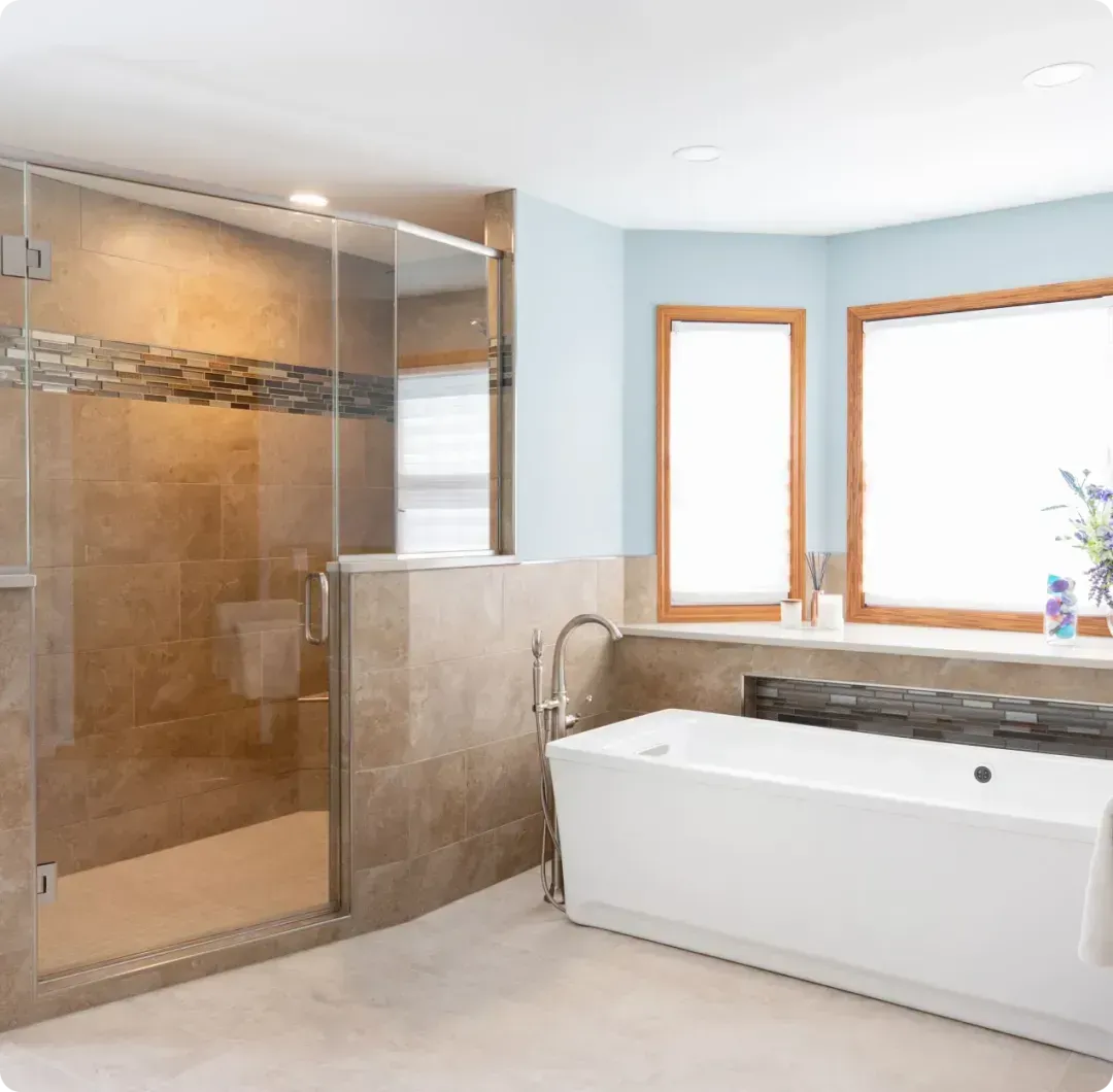 Modern bathroom with glass shower, white tub, and light blue walls beside two windows