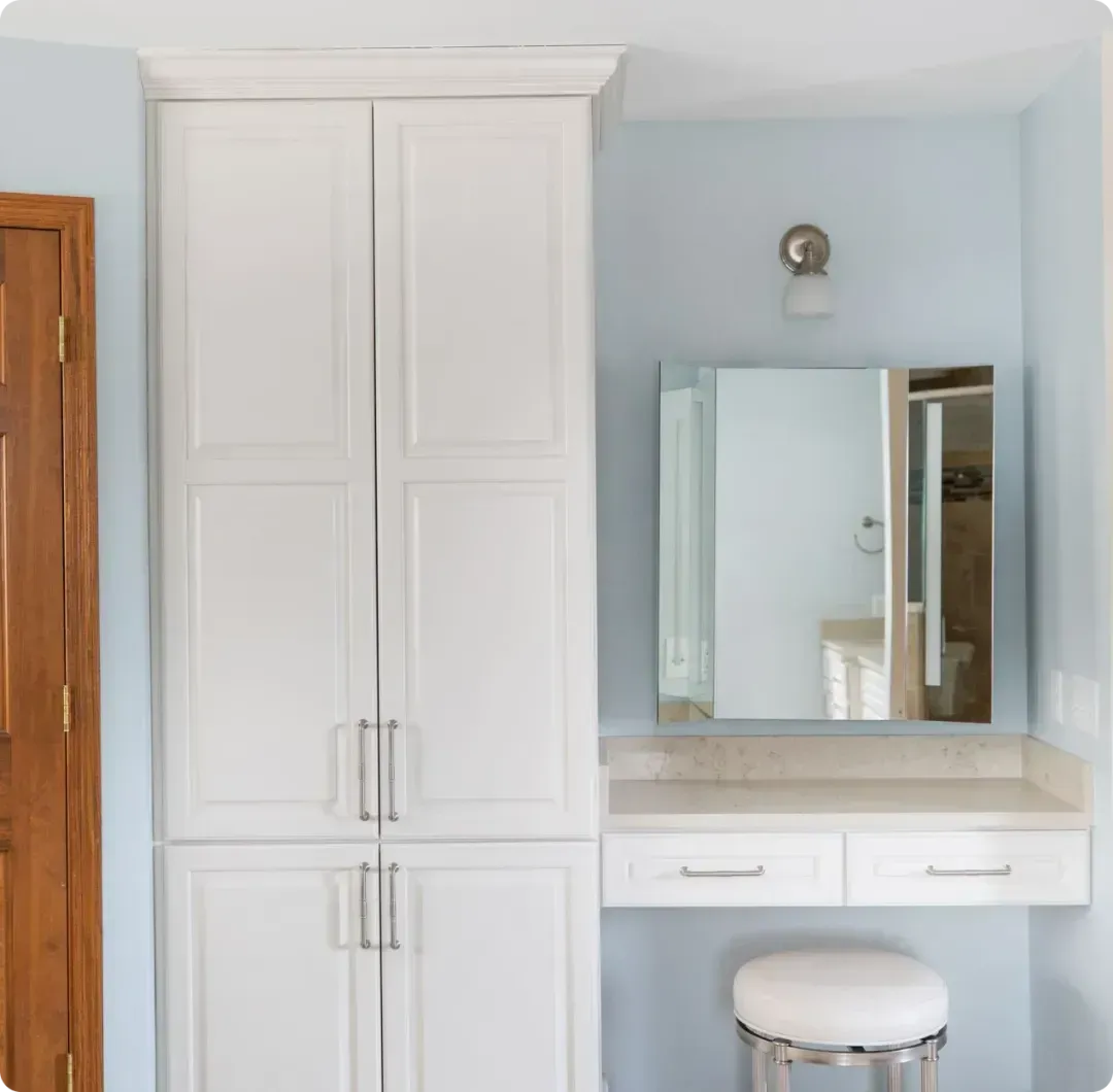 White built-in cabinets and vanity with mirror in a light blue bathroom room.