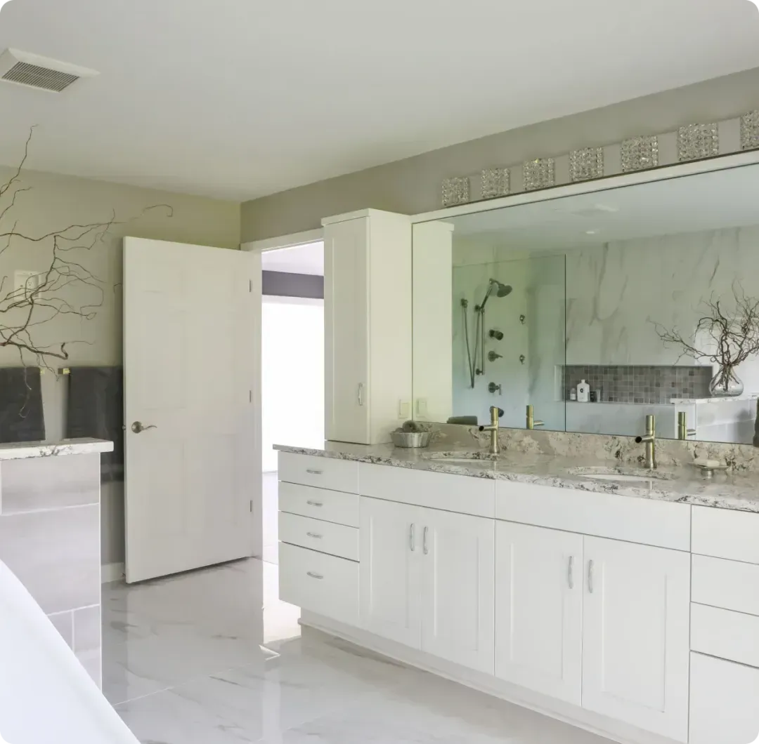 Bright white bathroom with double vanity, large mirror, and open door to a lit adjoining room