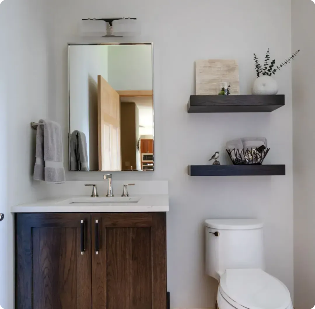 Modern bathroom with mirrored vanity, dark wood cabinet, toilet, and wall shelves with decor
