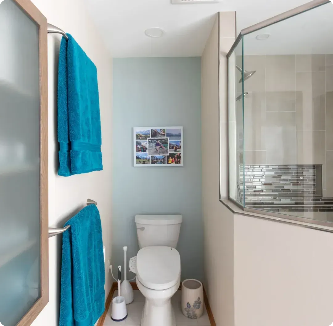 Small bathroom with white toilet, blue towels, and glass shower door.