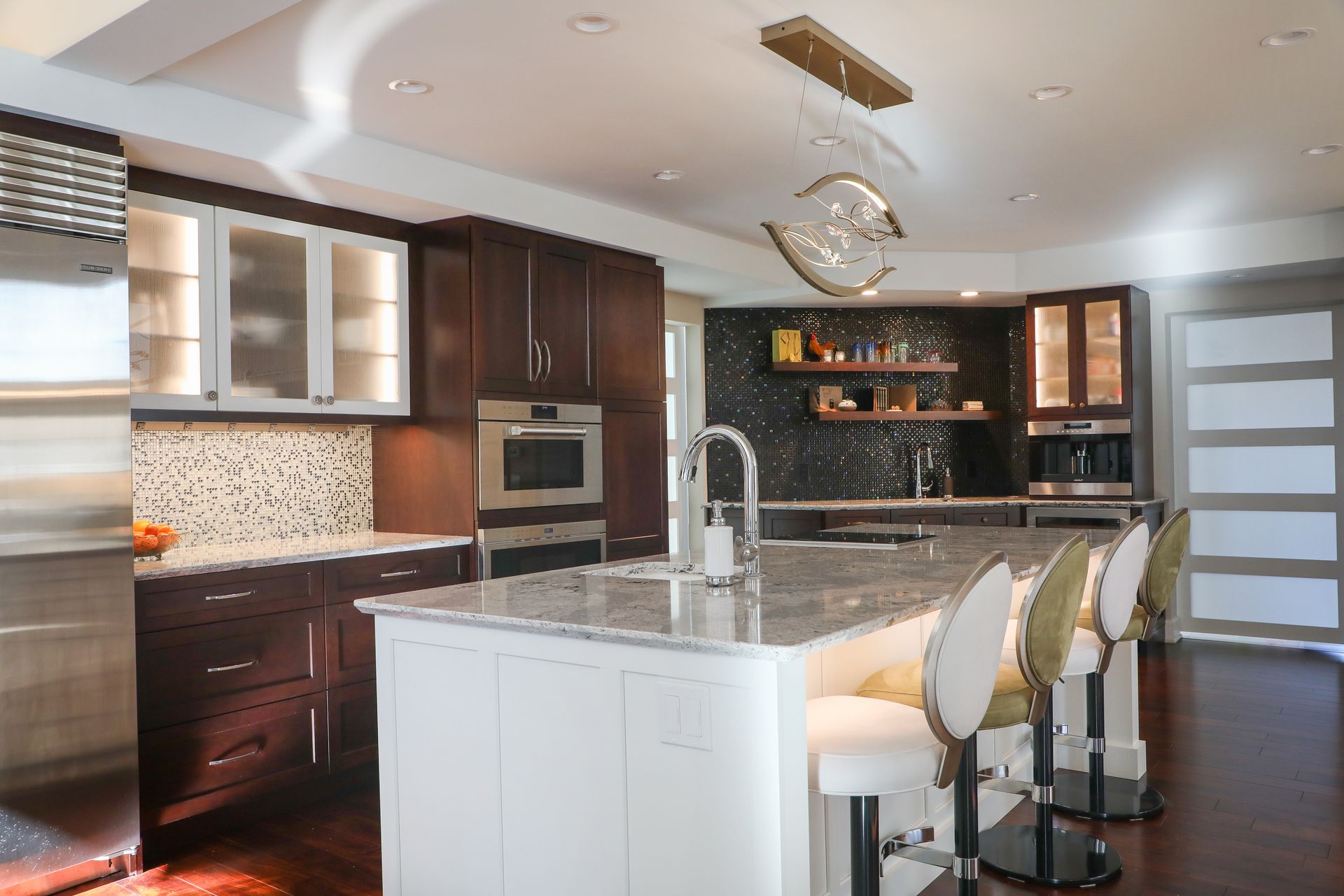 Modern kitchen with white island, dark wood cabinets, granite counters, and three bar stools