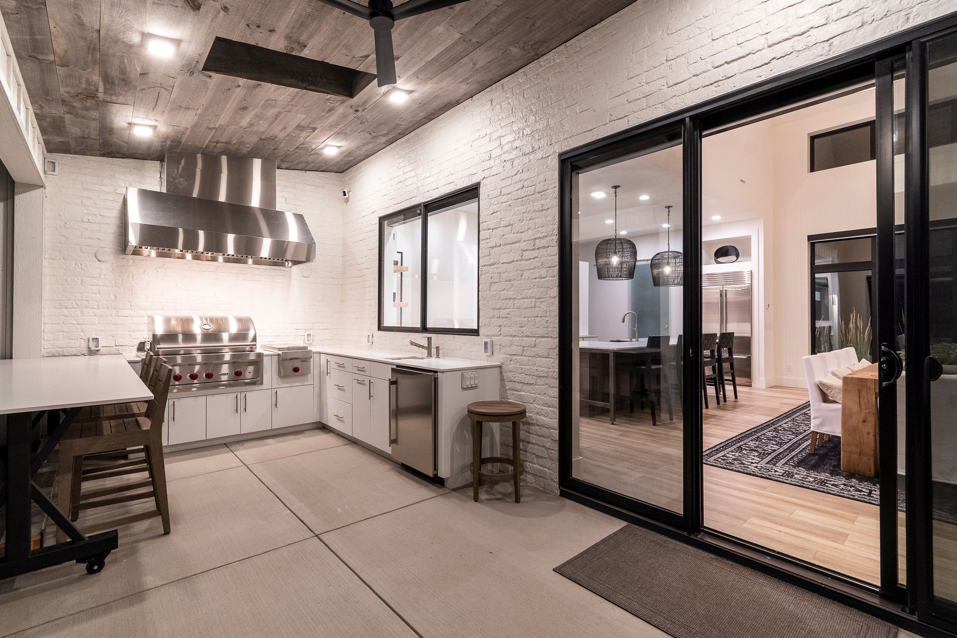 Modern kitchen and dining patio with white brick walls, black-framed glass doors, and stainless steel appliances