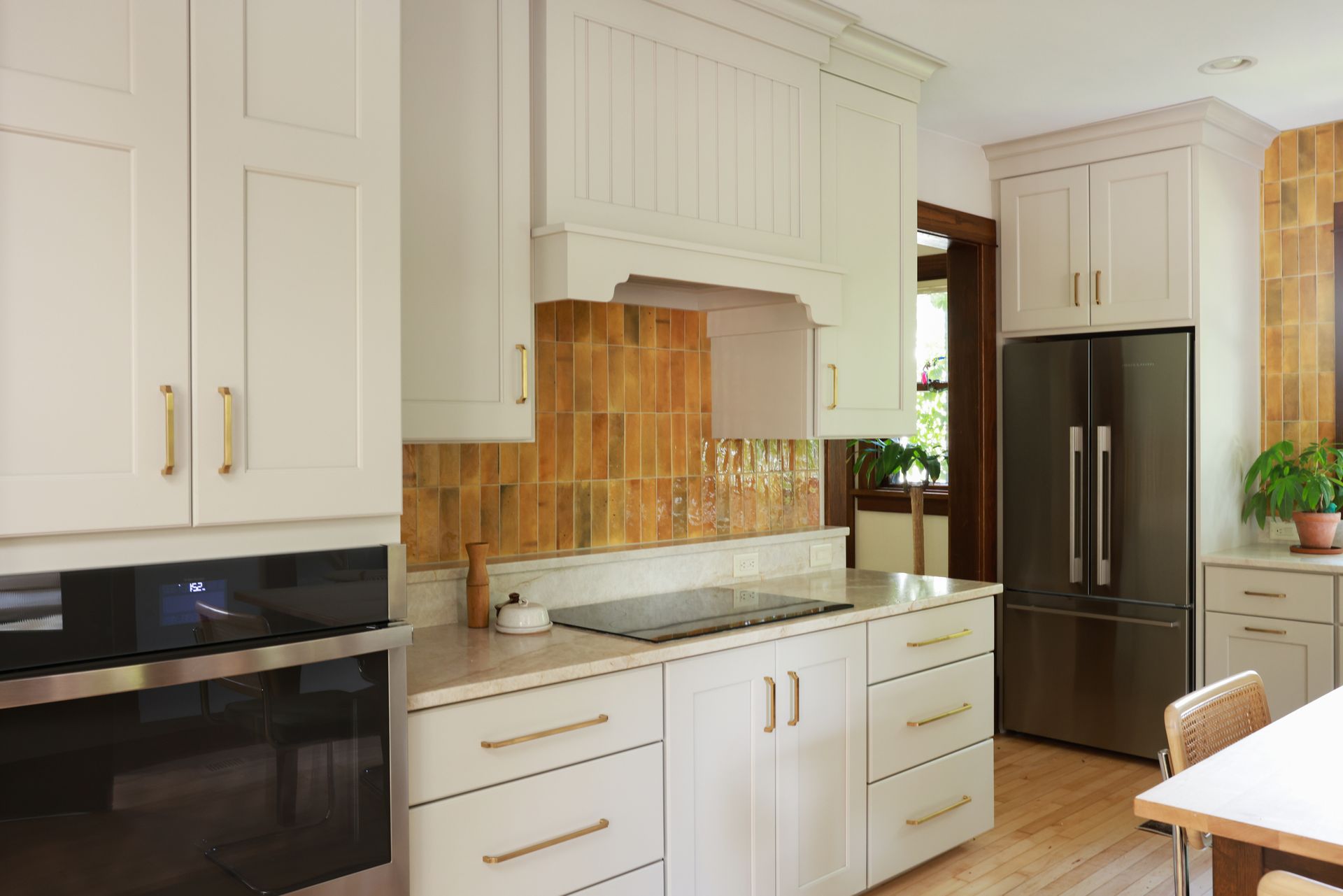 Bright kitchen with white cabinets, orange tile backsplash, black built-in oven, and stainless steel fridge.