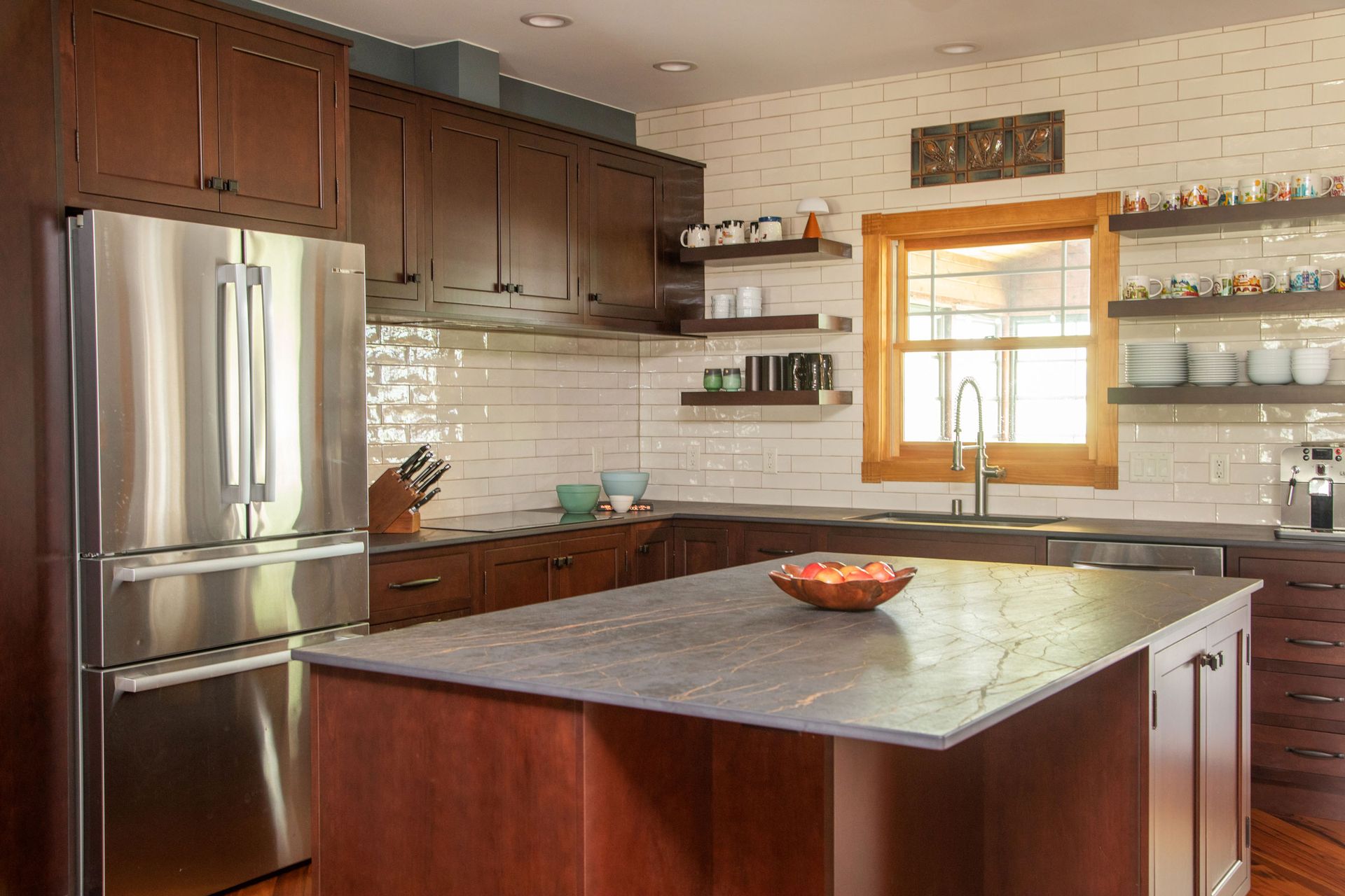 Modern kitchen with stainless steel fridge, dark wood cabinets, marble island, and window shelves