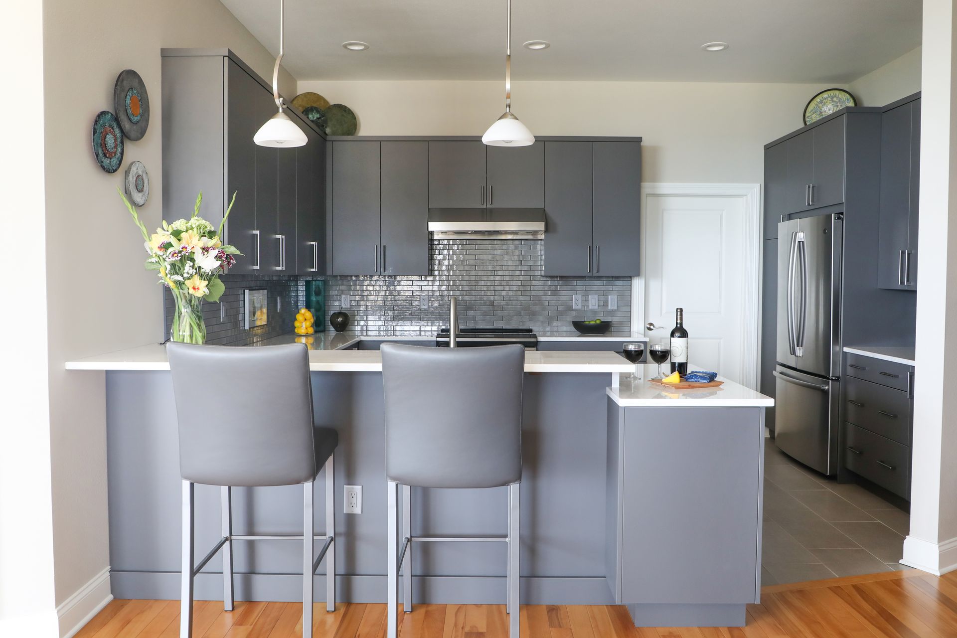 Modern kitchen with gray cabinets, island seating, pendant lights, and stainless steel appliances