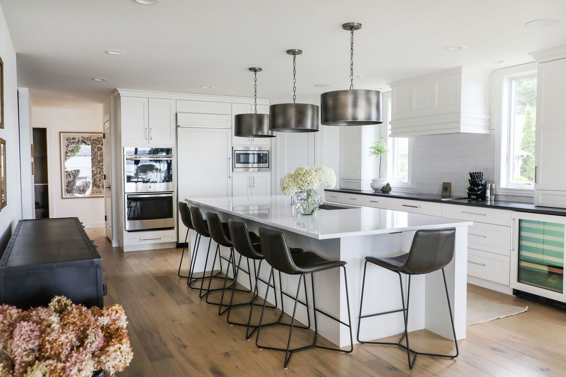 Bright modern kitchen with white island, black barstools, pendant lights, and wood floors