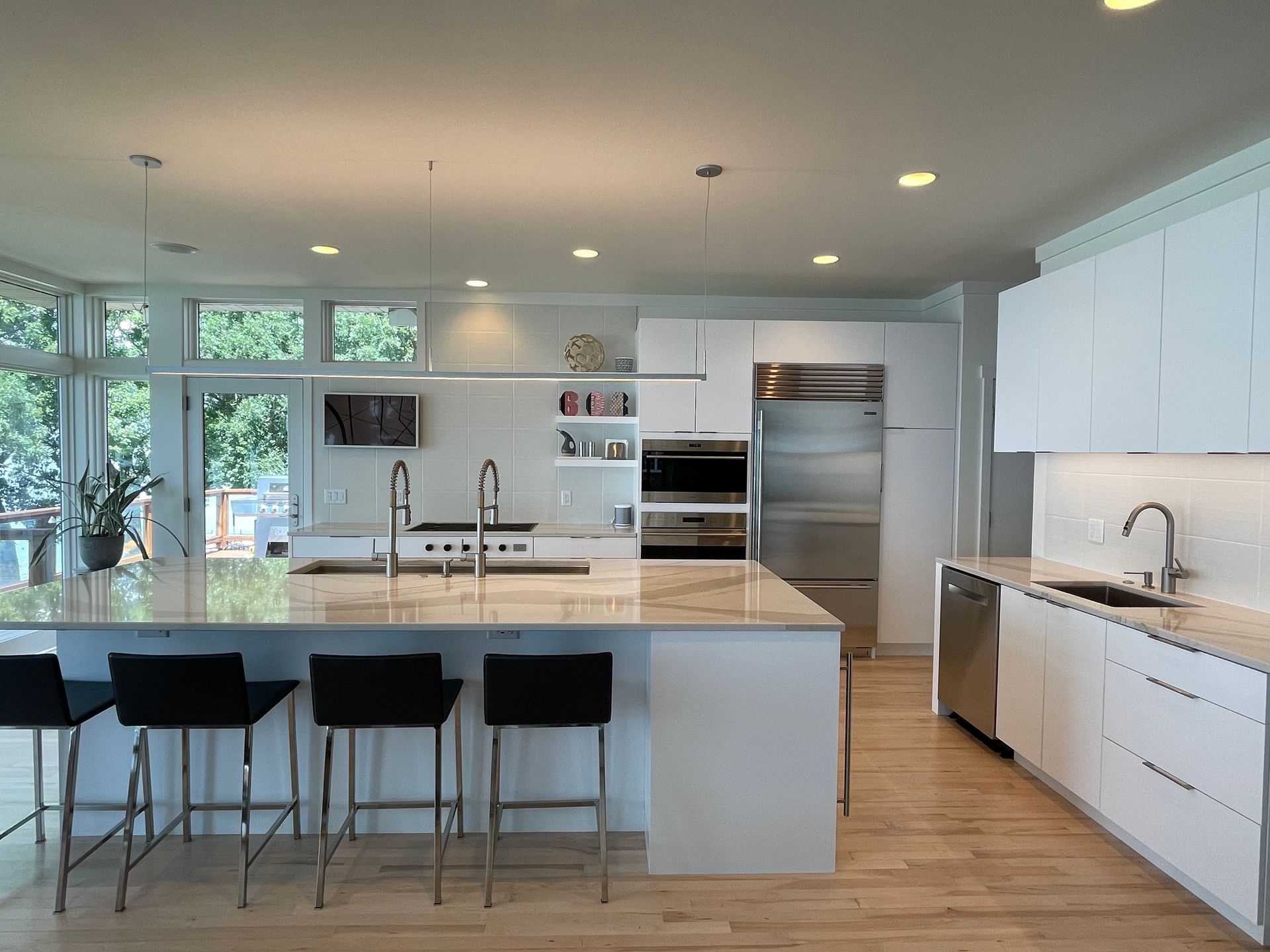 Bright modern kitchen with white cabinets, large island, stools, and stainless steel appliances