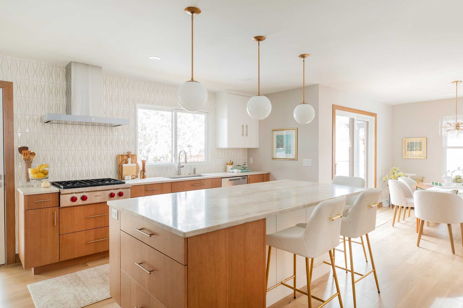 Bright modern kitchen with island, white cabinets, pendant lights, and dining table by the windows