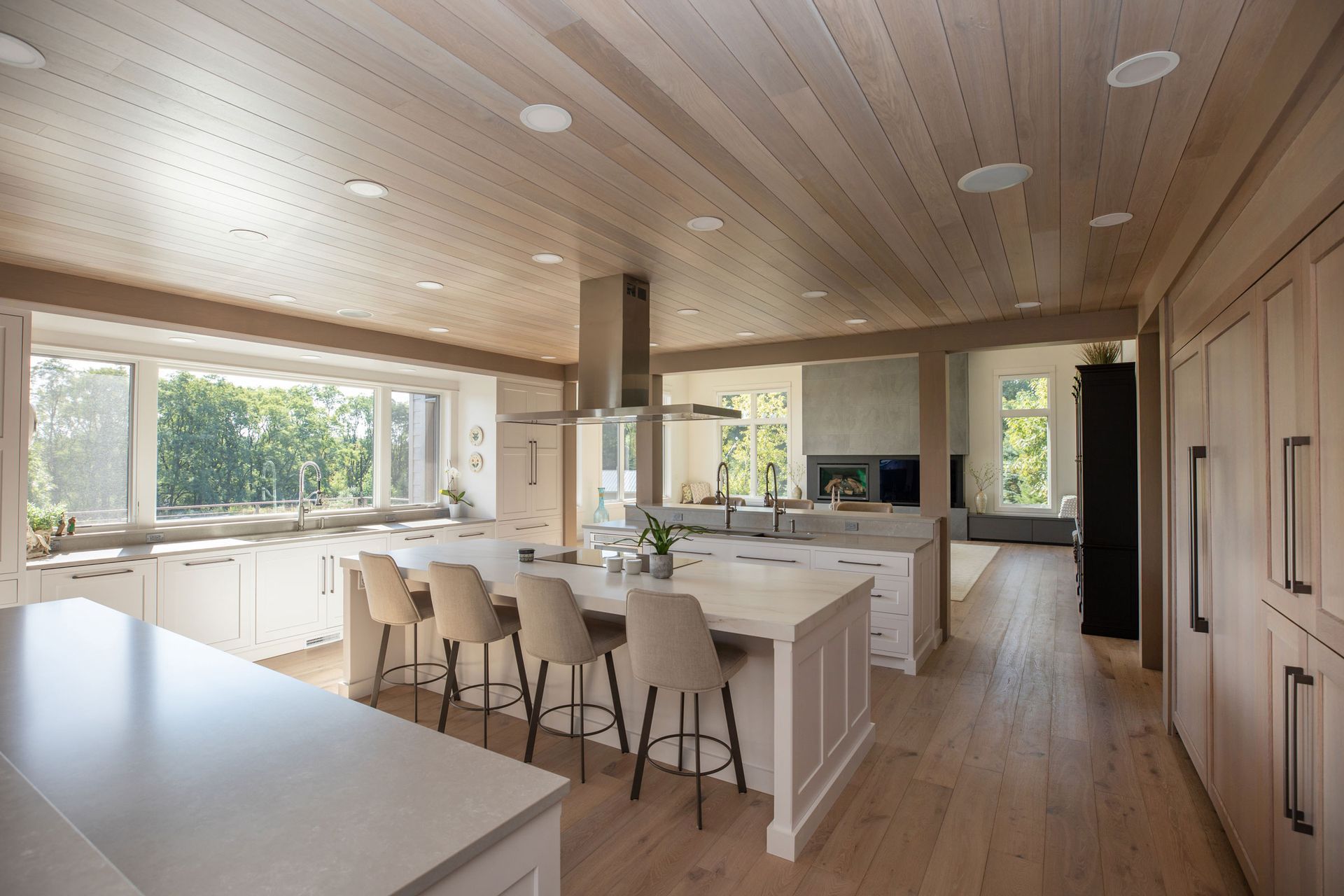 Modern kitchen with island seating, light wood cabinets, and large windows overlooking greenery