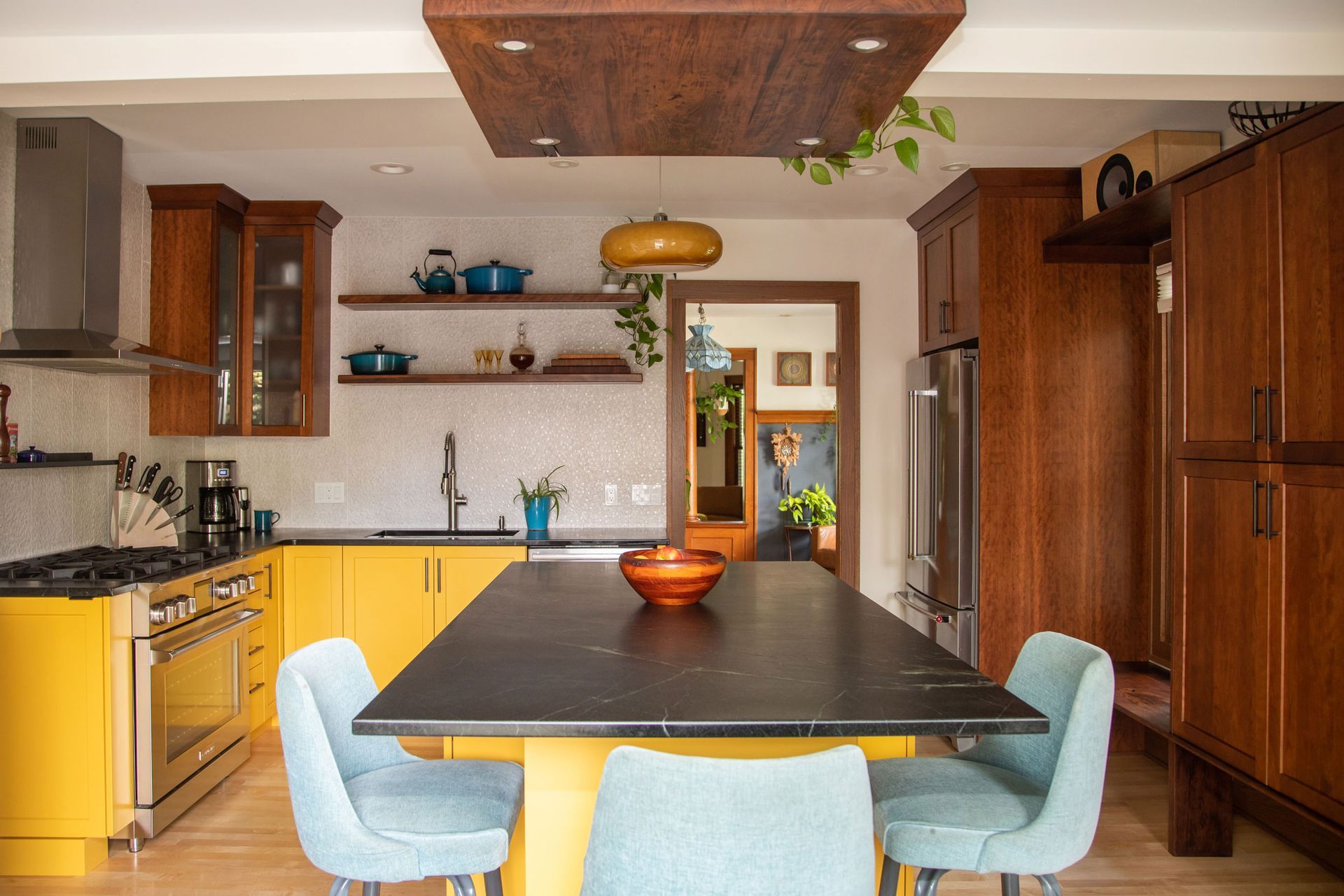 Modern kitchen with yellow cabinets, wooden island, and light blue chairs on a bright rug