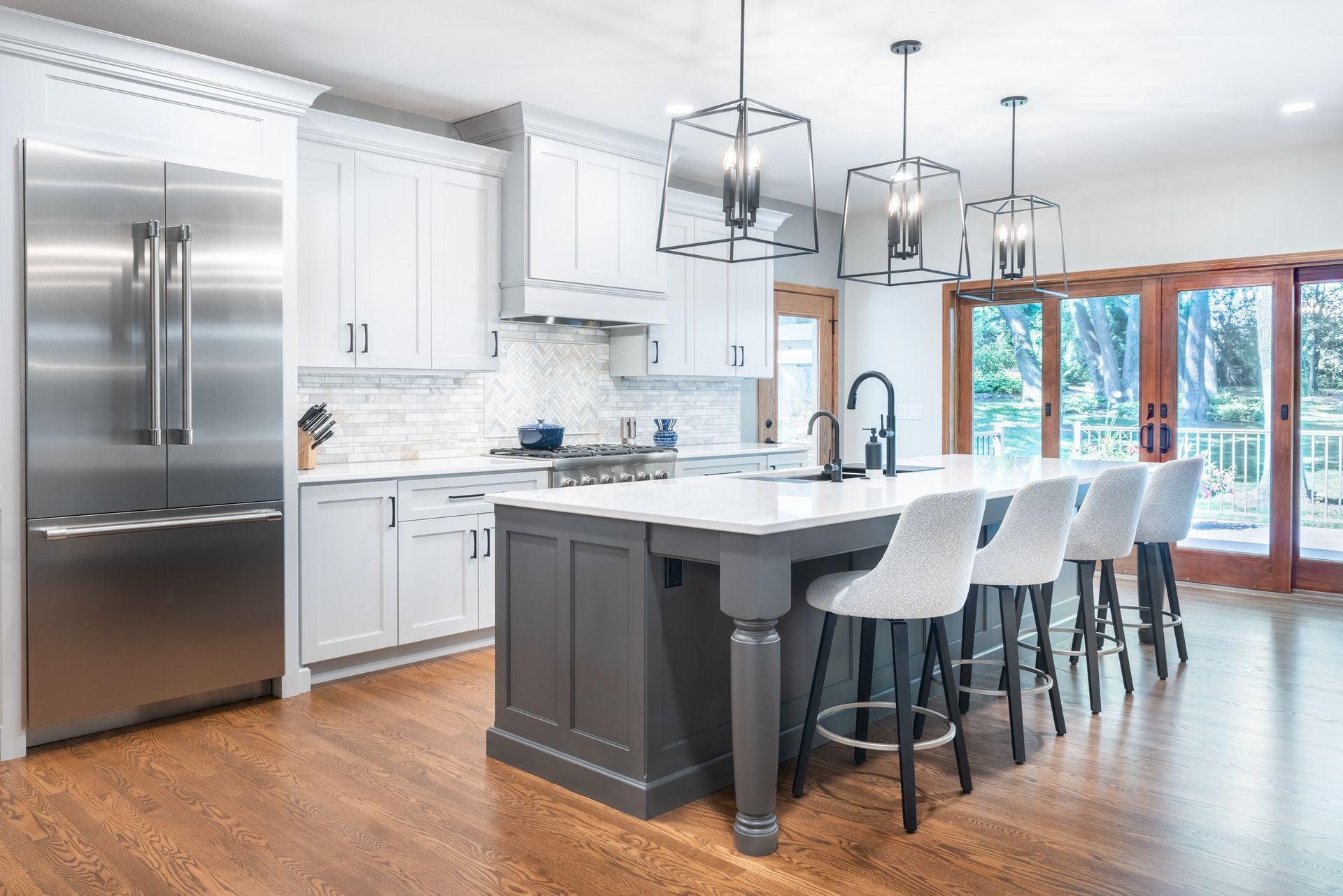 Bright modern kitchen with white cabinets, stainless fridge, island, and bar stools by large windows