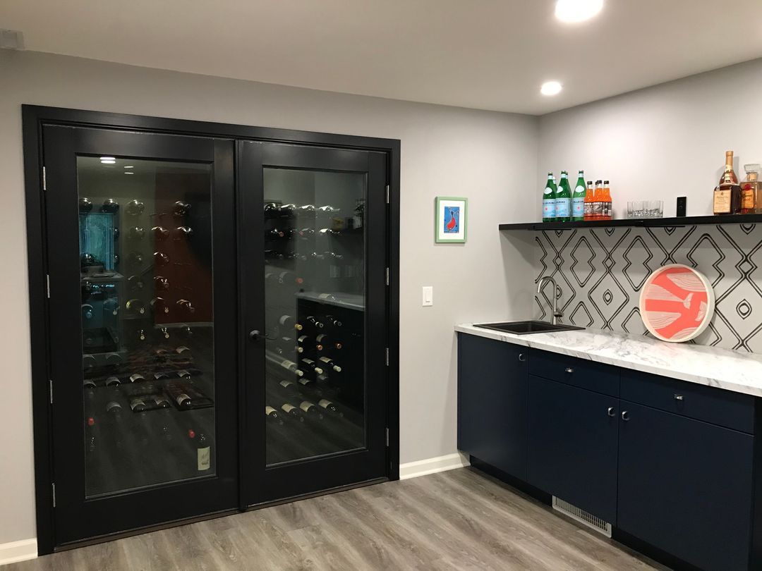 Modern home bar with black wine fridge, navy cabinets, white countertop, and patterned backsplash