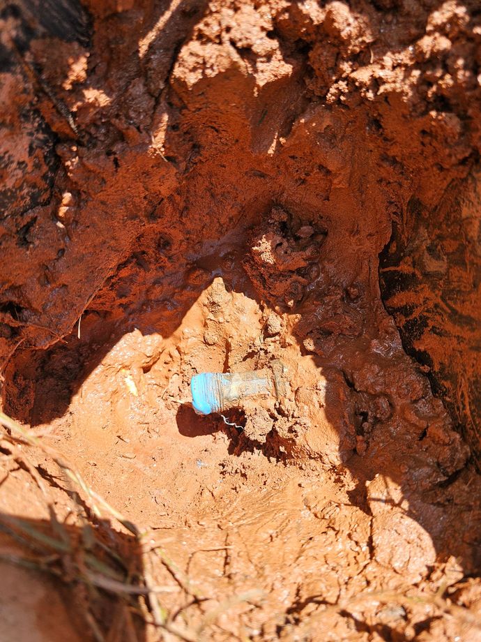Close-up of a small blue object lodged in reddish-brown soil and rocks.