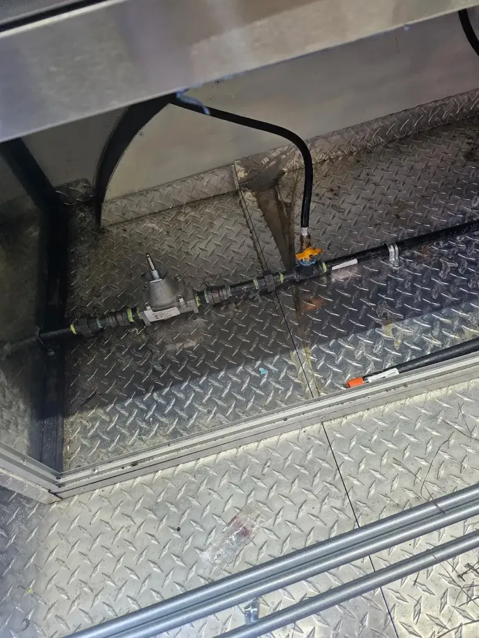 Metal diamond-plate truck bed with black support frame and hoses beneath a raised metal surface.