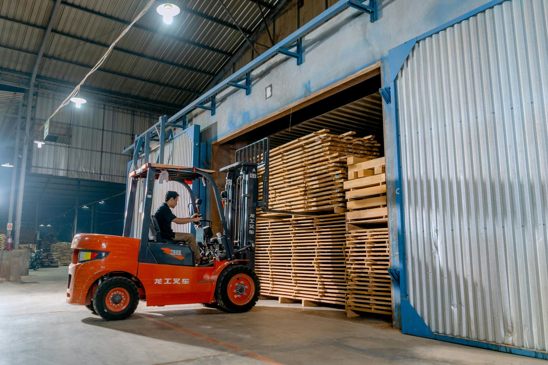 A man is driving a forklift in a warehouse filled with wooden pallets.