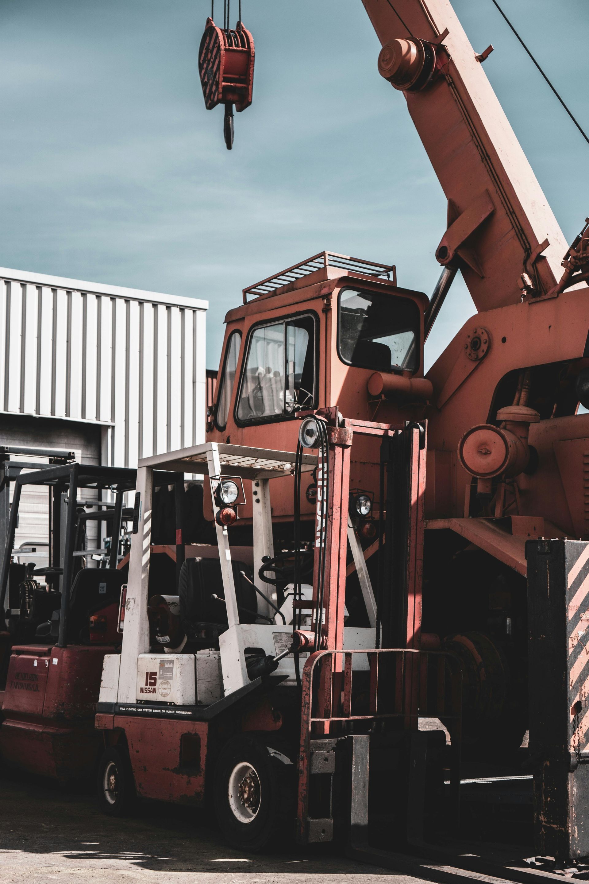A forklift and a crane are parked in front of a building.