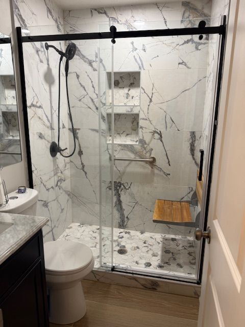 A modern walk-in shower with white marble-patterned walls, black fixtures, a wooden fold-down seat, and glass doors.