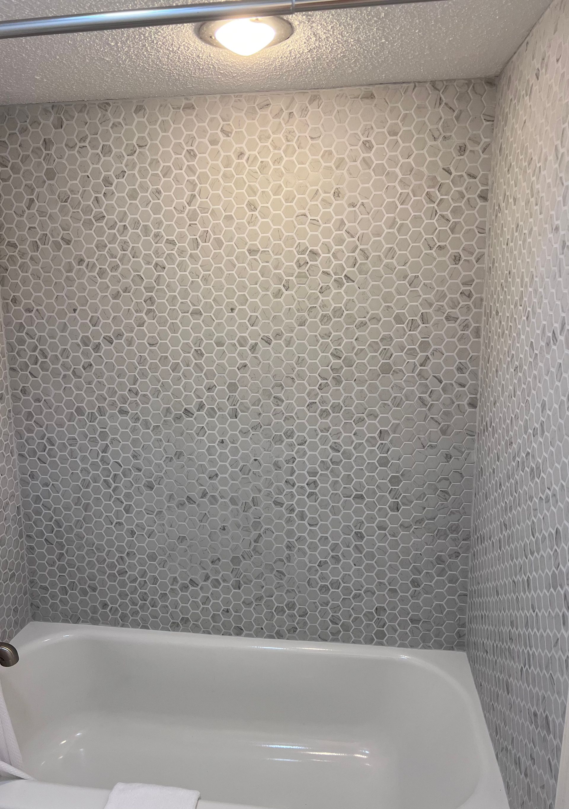 A bathtub with a white basin set against a wall featuring patterned, grey-and-white hexagonal mosaic tiles.