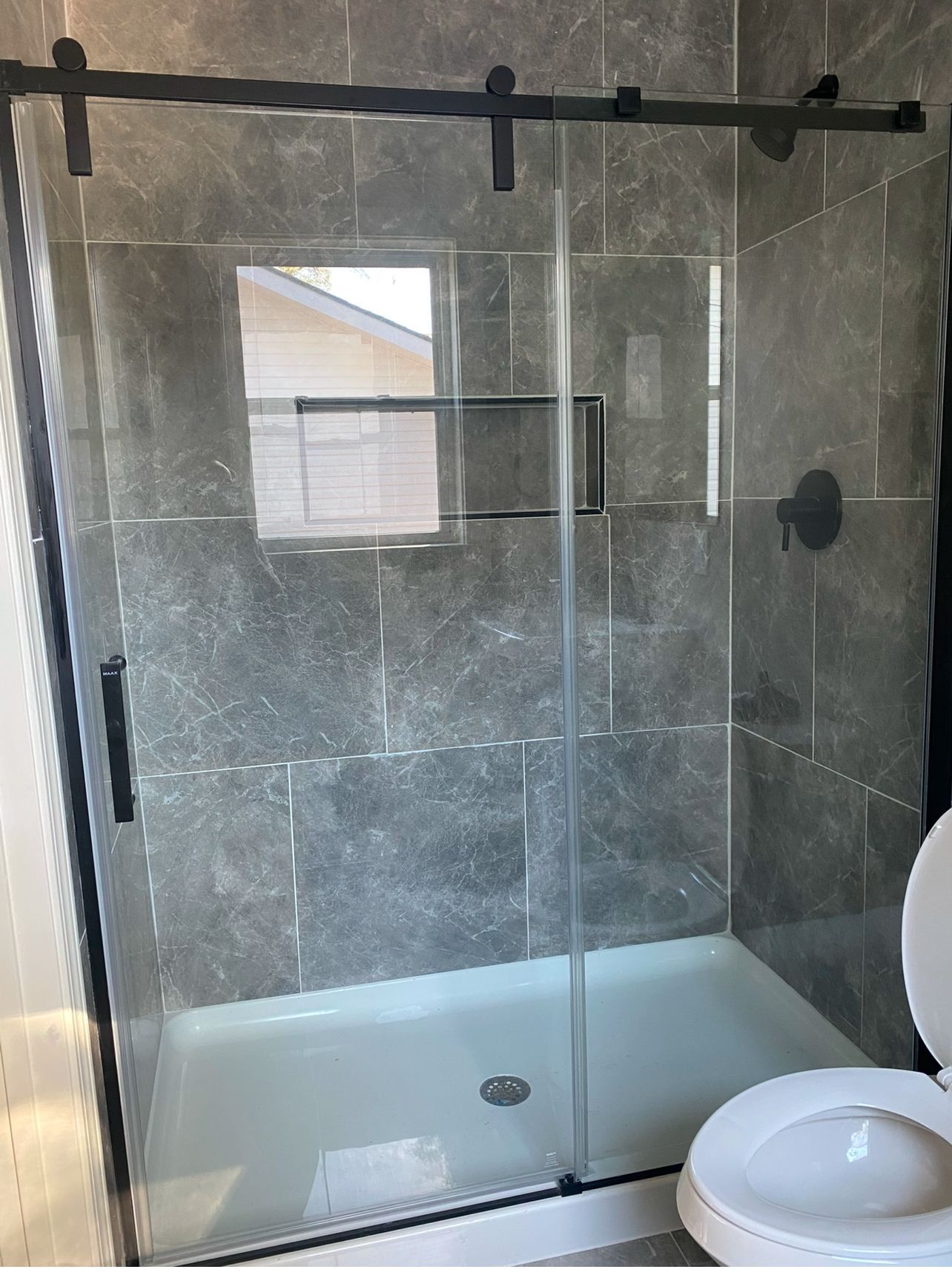 A modern glass shower enclosure with sliding doors installed against grey tiled walls in a bathroom.