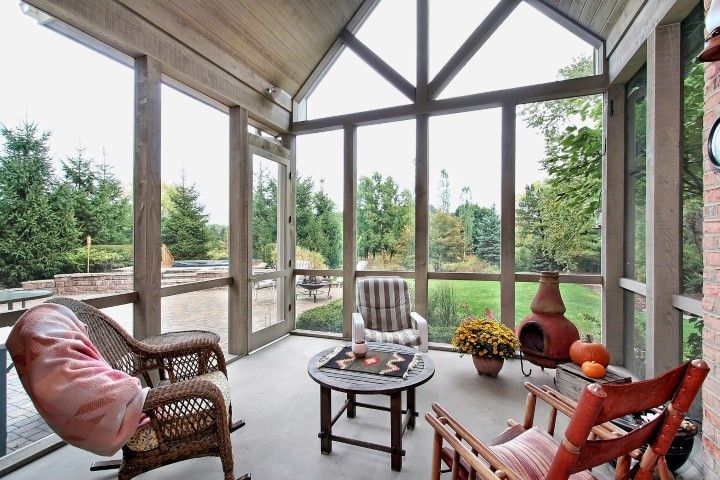 Sunroom with wicker chairs, small table, and pumpkin decor overlooking a tree-lined yard.