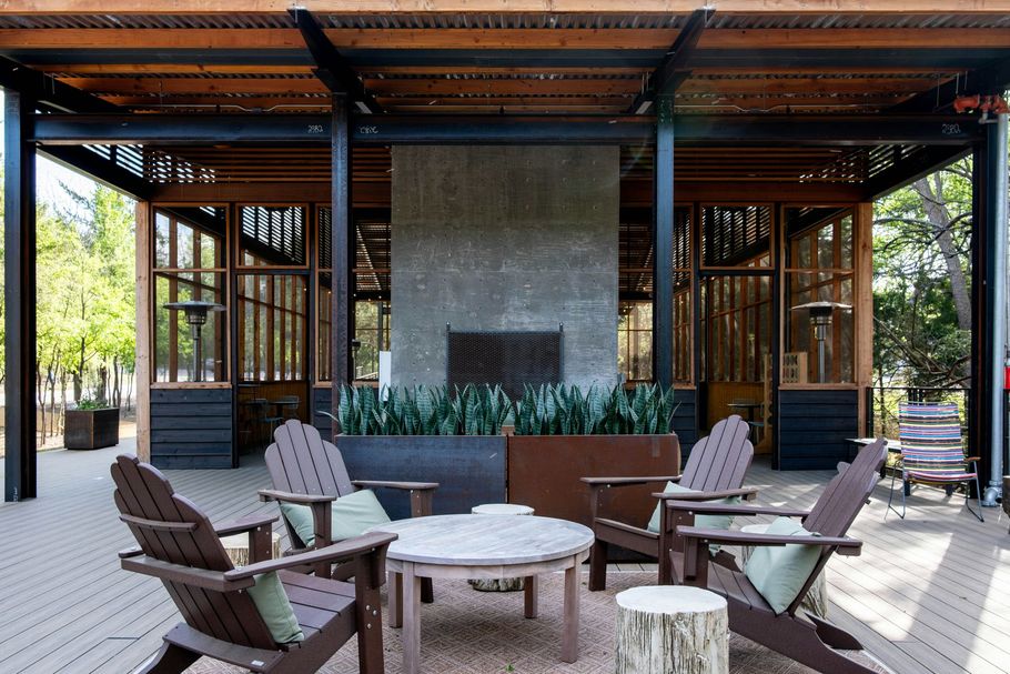 Outdoor patio with wooden chairs around a fire pit and stone fireplace under a covered pavilion