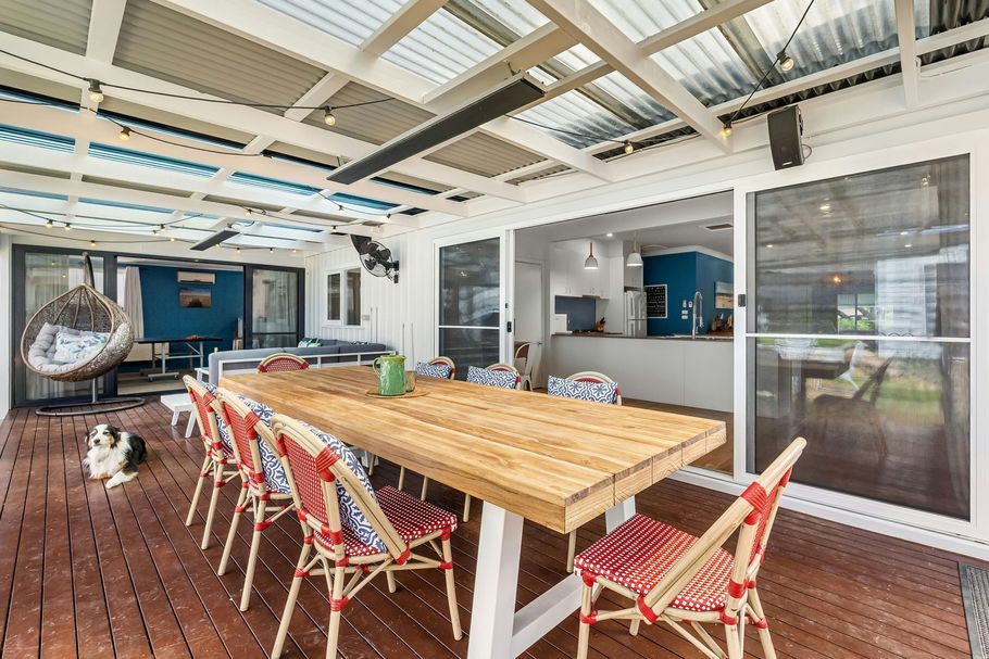 Covered patio with wooden dining table, red chairs, and sliding glass doors to a blue kitchen.
