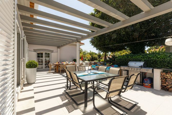 Sunny outdoor patio with pergola, dining table, lounge chairs, and poolside seating