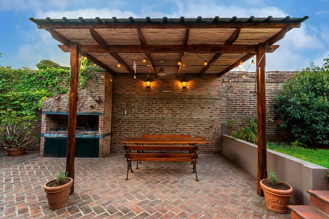 Covered patio with wooden bench, brick wall, potted plants, and warm hanging lights.