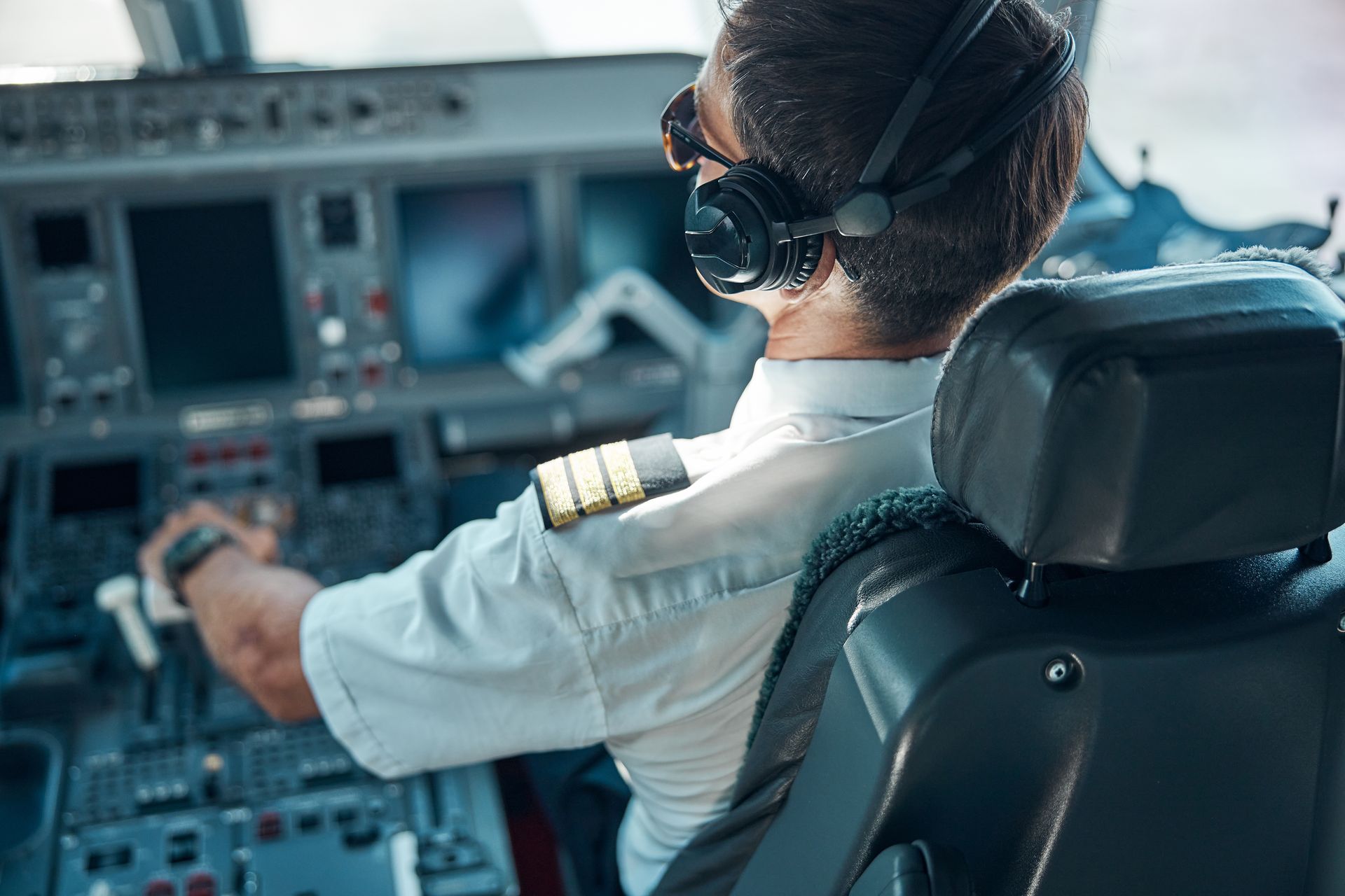 Pilot in cockpit, wearing headphones and sunglasses, manipulating controls.