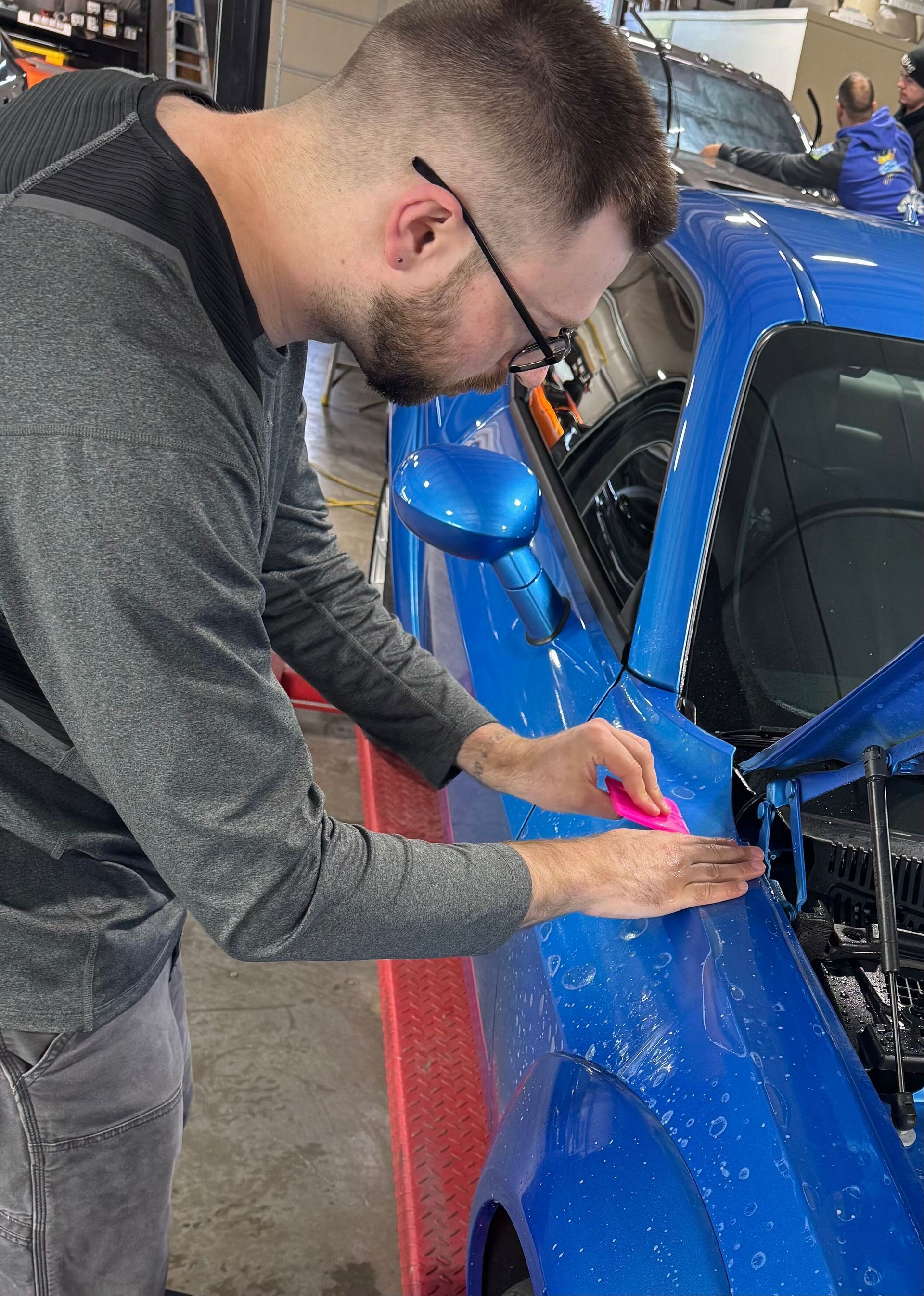 A man is working on a blue car in a garage.