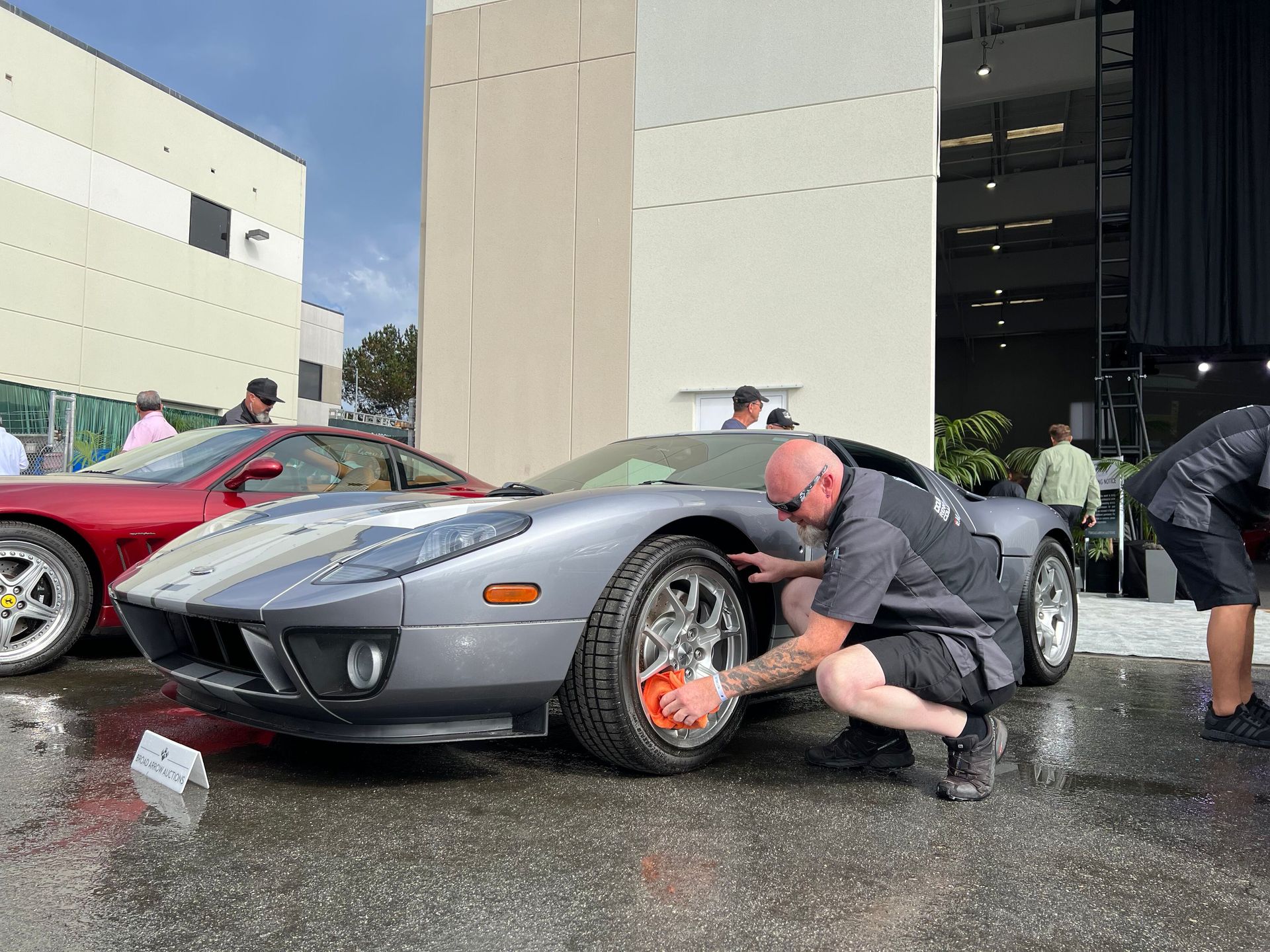 A man is kneeling down to wash a sports car.