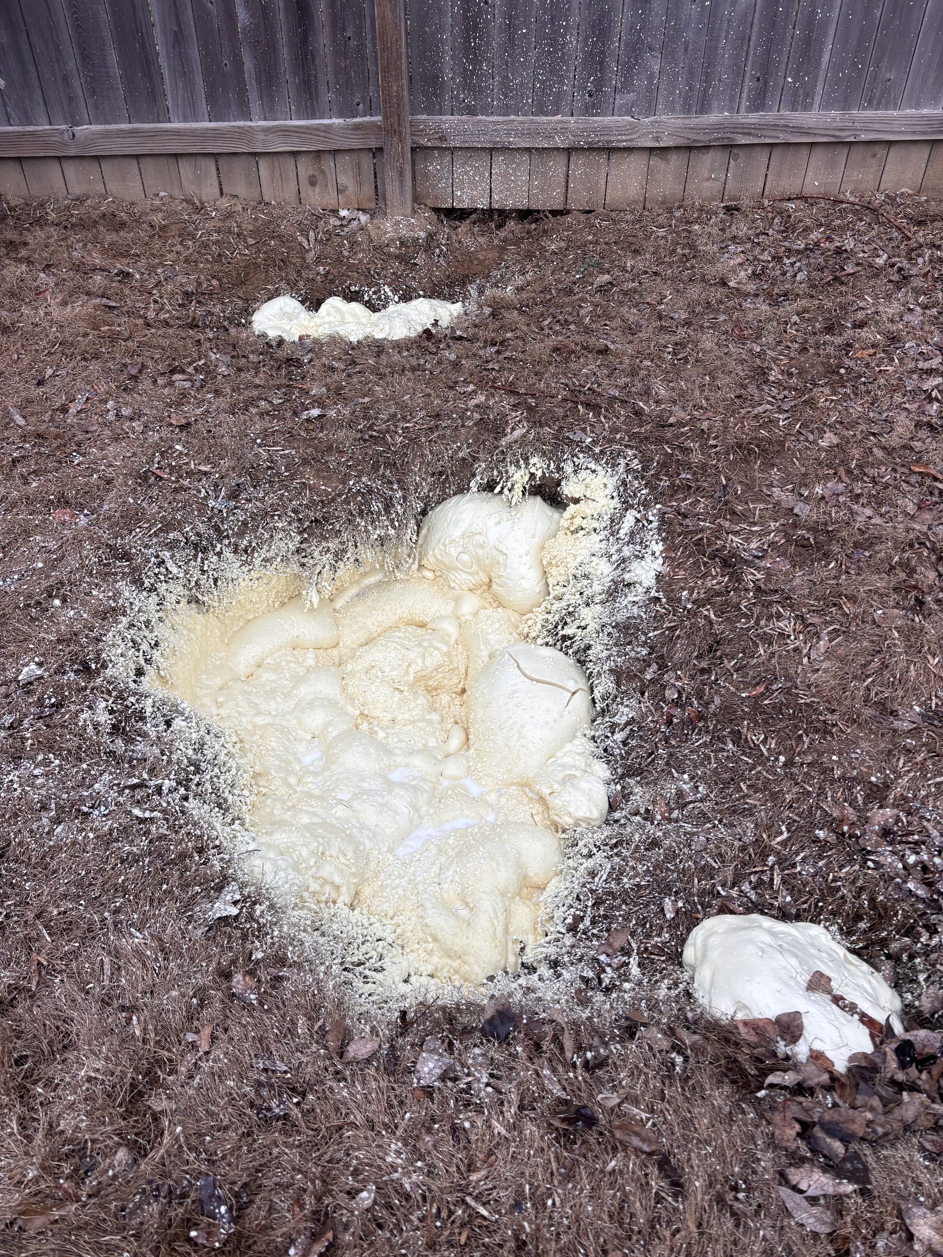 A construction worker in a yellow hard hat and grey uniform uses a spirit level on a concrete curb at a building site.