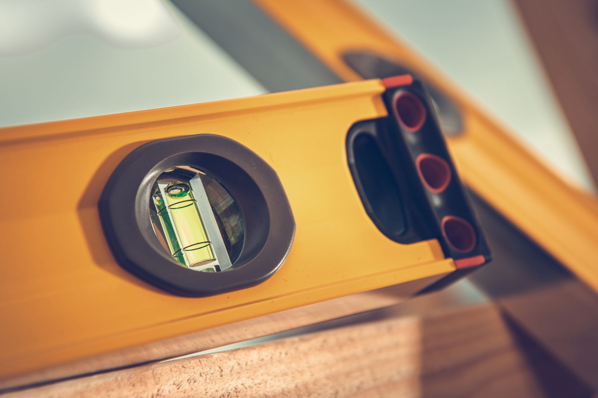 A bright yellow spirit level resting on a wooden surface, showing the centered bubble in the vial.