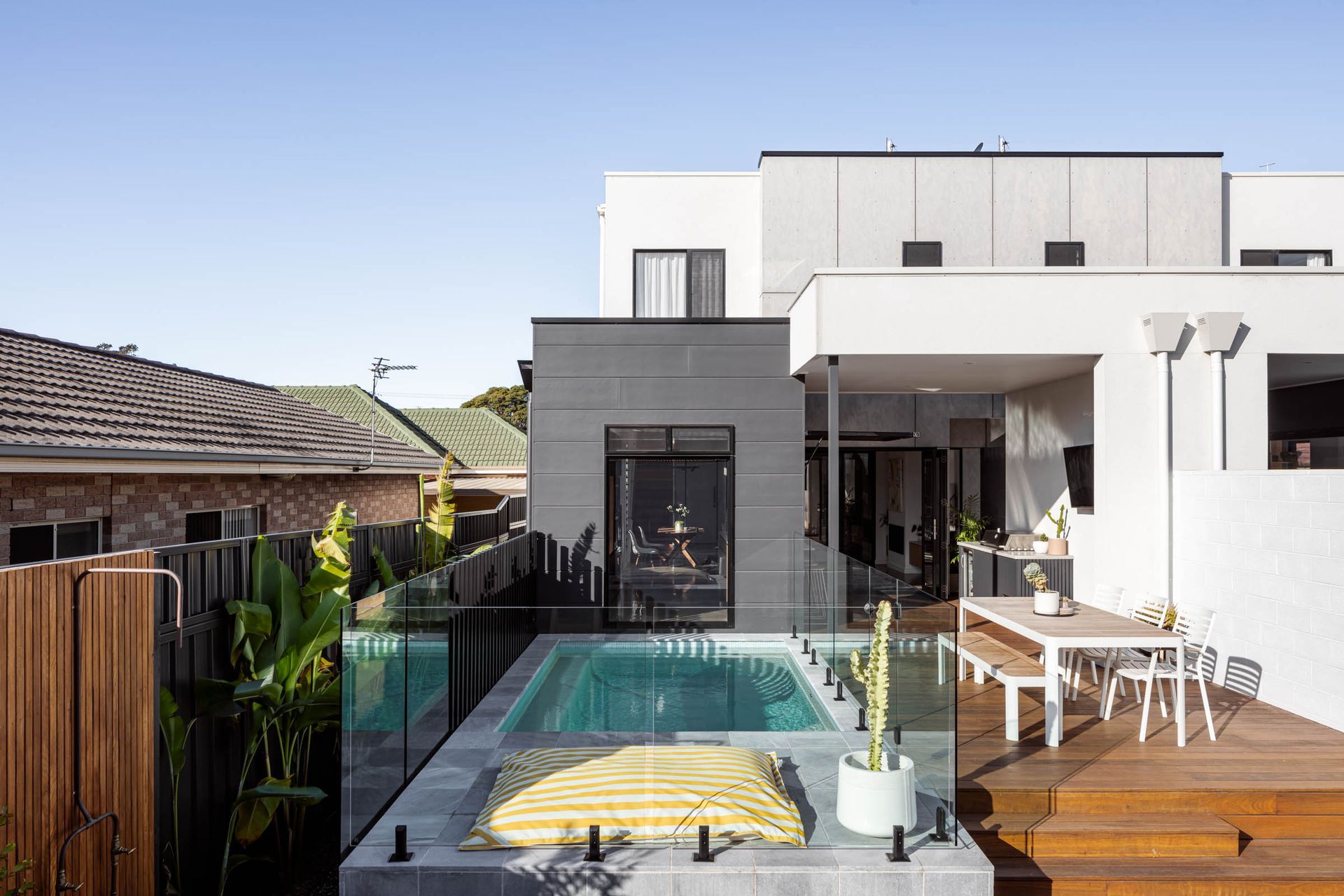 Modern backyard with a pool, deck, and a two-story white house. — Goode By Design in Unanderra, NSW