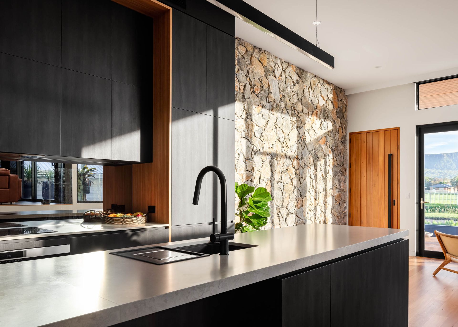 Modern kitchen with dark cabinets, stone wall, and metal countertop. — Goode By Design in Unanderra, NSW