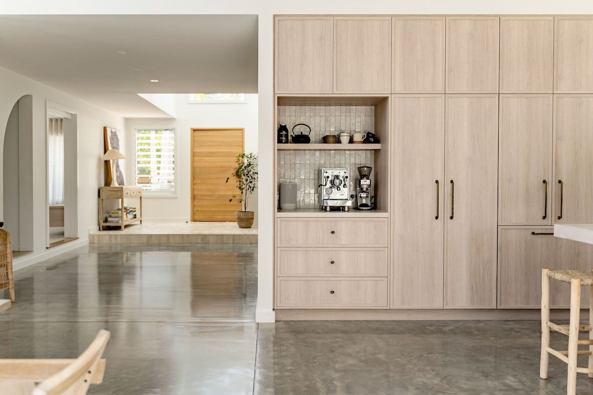 Light wood cabinets with coffee station in modern, open-concept kitchen. Polished concrete floor, arched doorway leads to hallway. — Goode By Design in Unanderra, NSW
