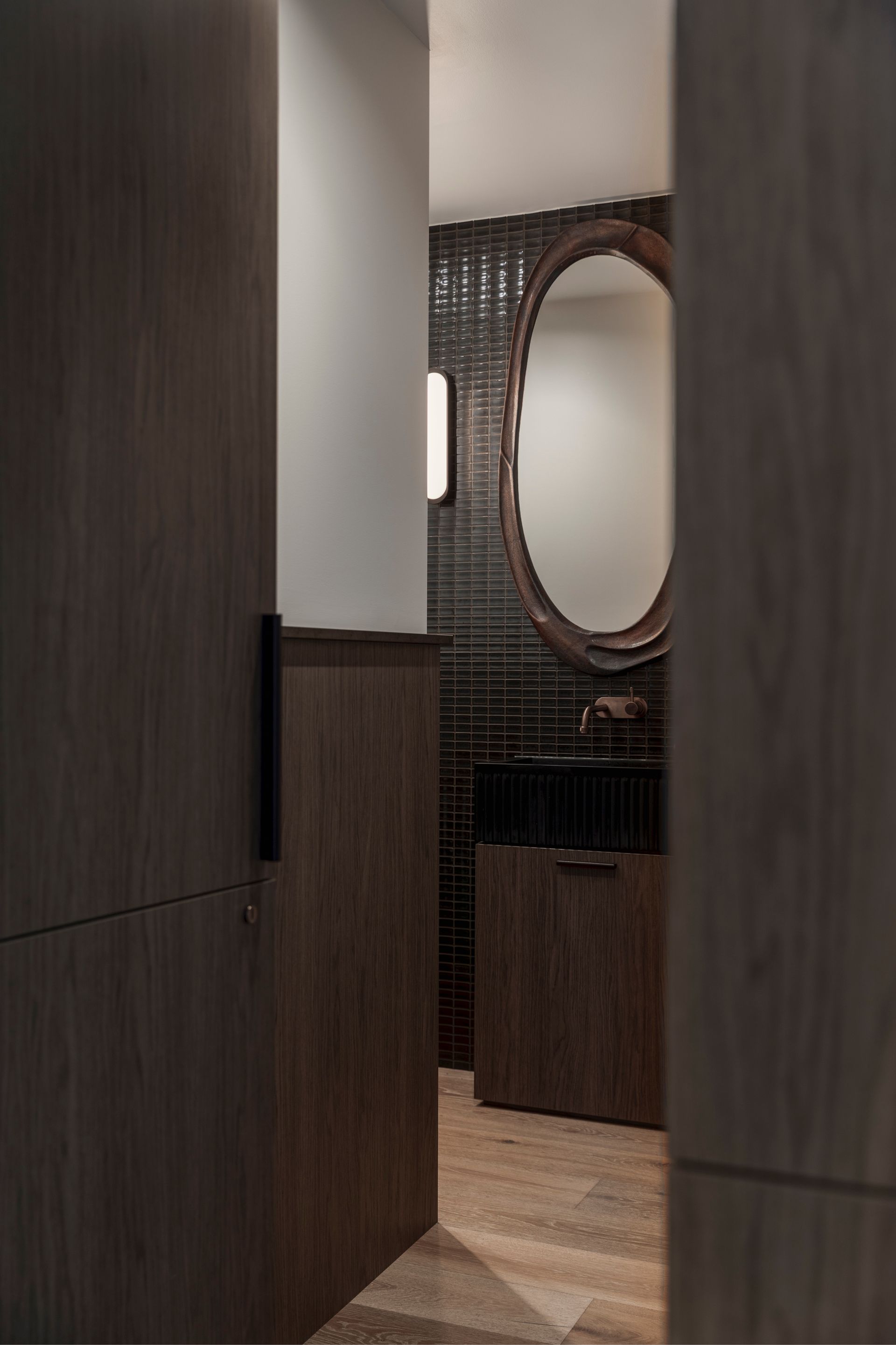 Narrow hallway with dark wood panels, a large oval mirror, and a small cabinet.