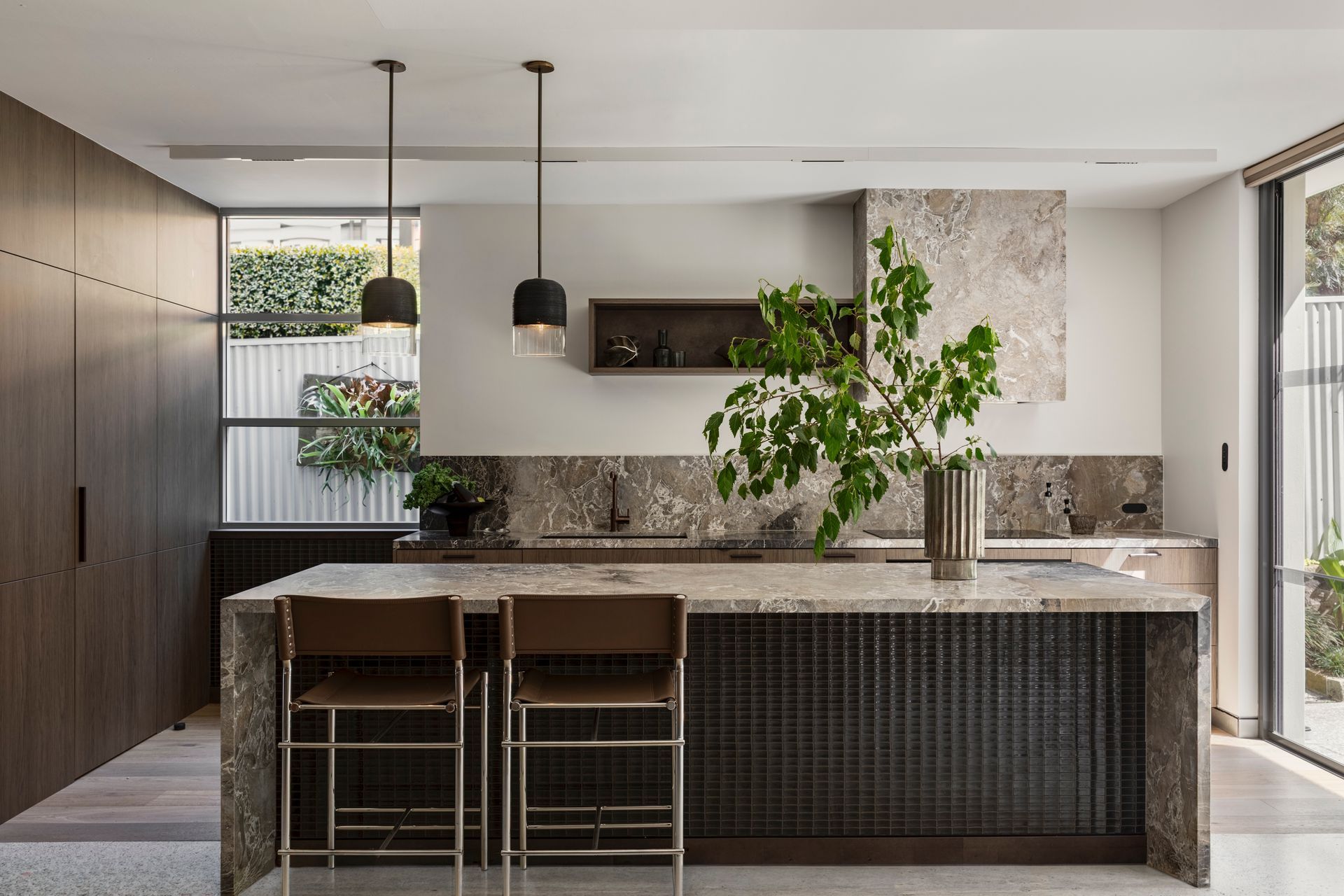 Modern kitchen with marble island, black pendant lights, and a plant by the window.