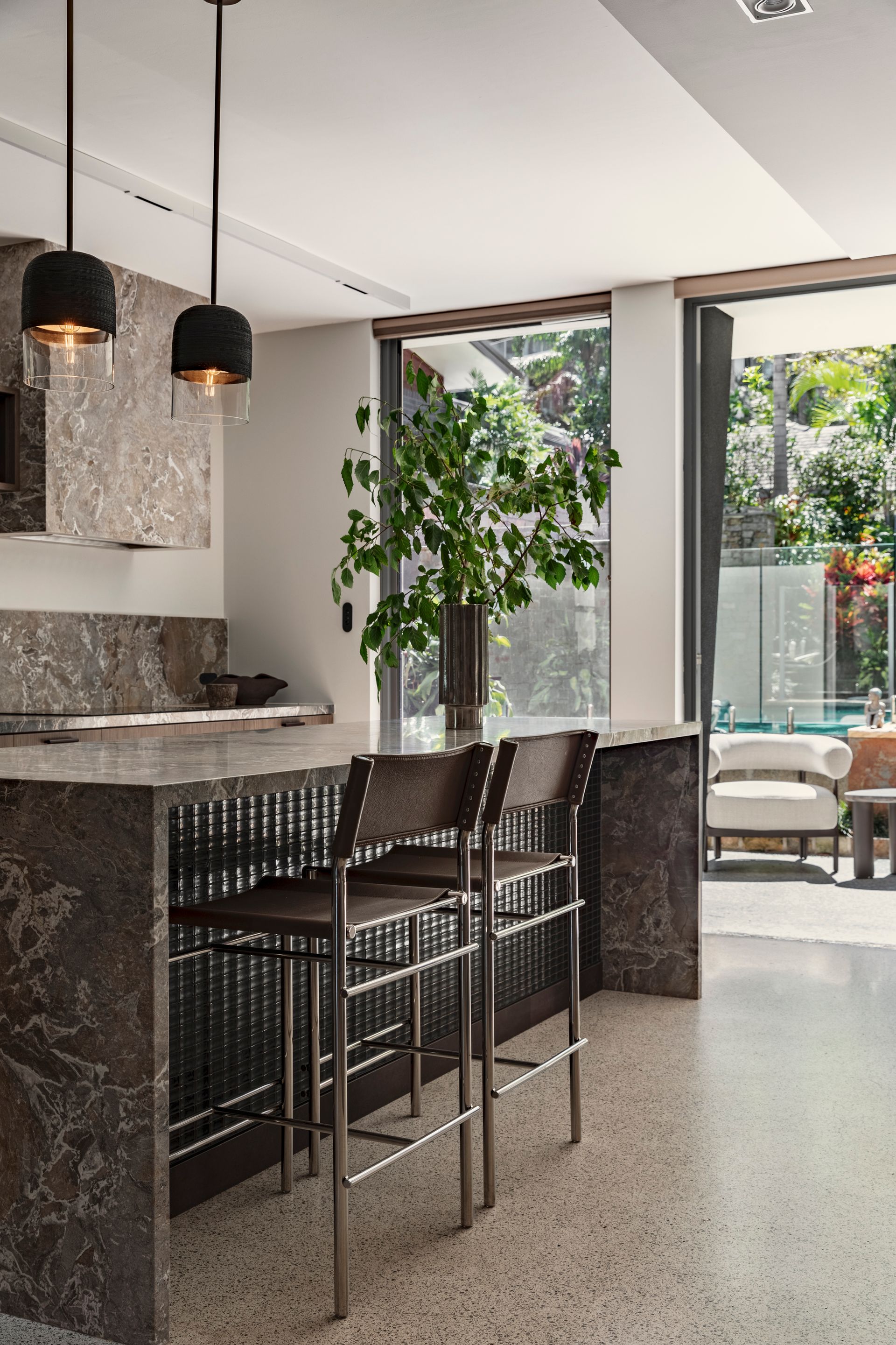 Modern kitchen with marble island, black bar stools, pendant lights, and large glass doors to a patio