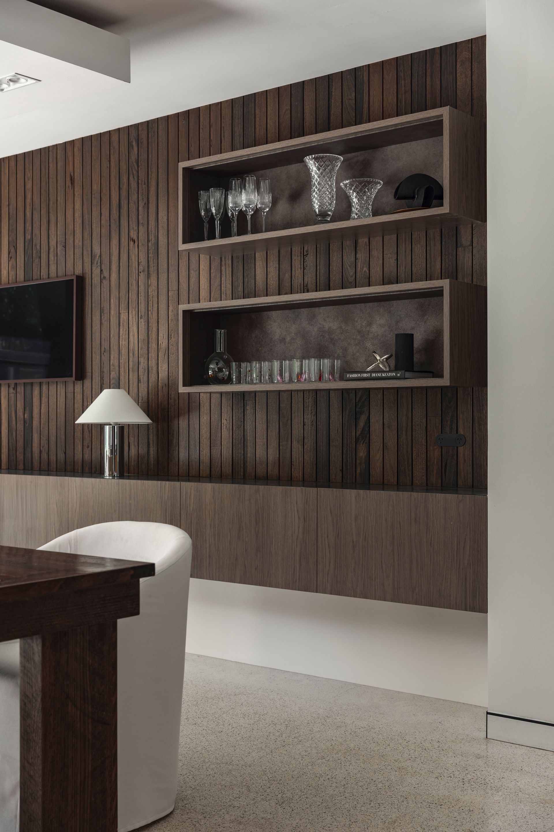 Modern living room with wood-paneled wall, built-in shelves, lamp, and white seating