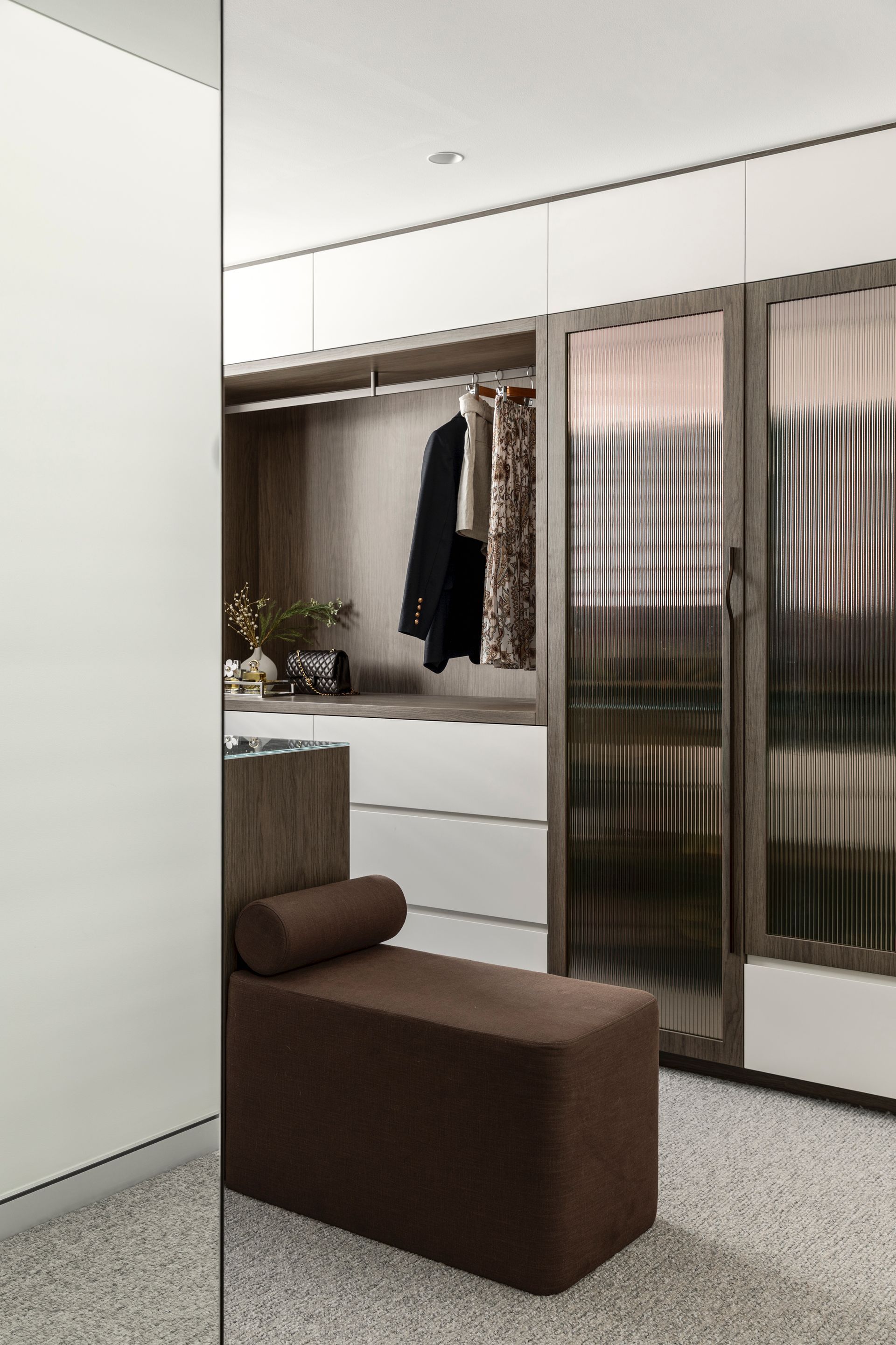 Modern bedroom with a brown chair, white wardrobe, and mirrored sliding closet doors