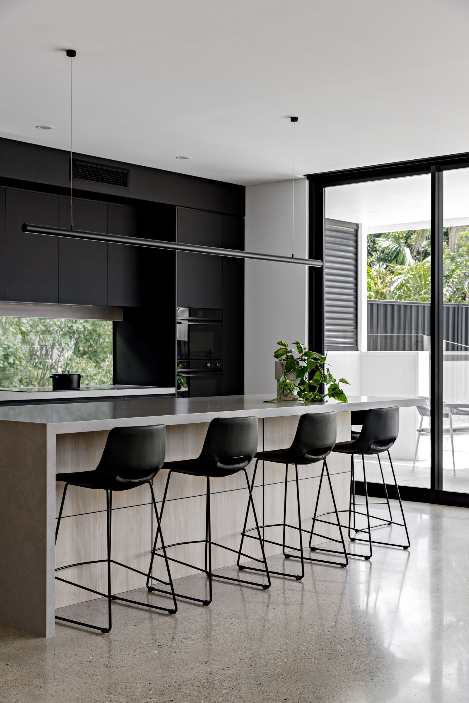 Modern kitchen with black cabinets, light countertops, and black bar stools. — Goode By Design in Unanderra, NSW