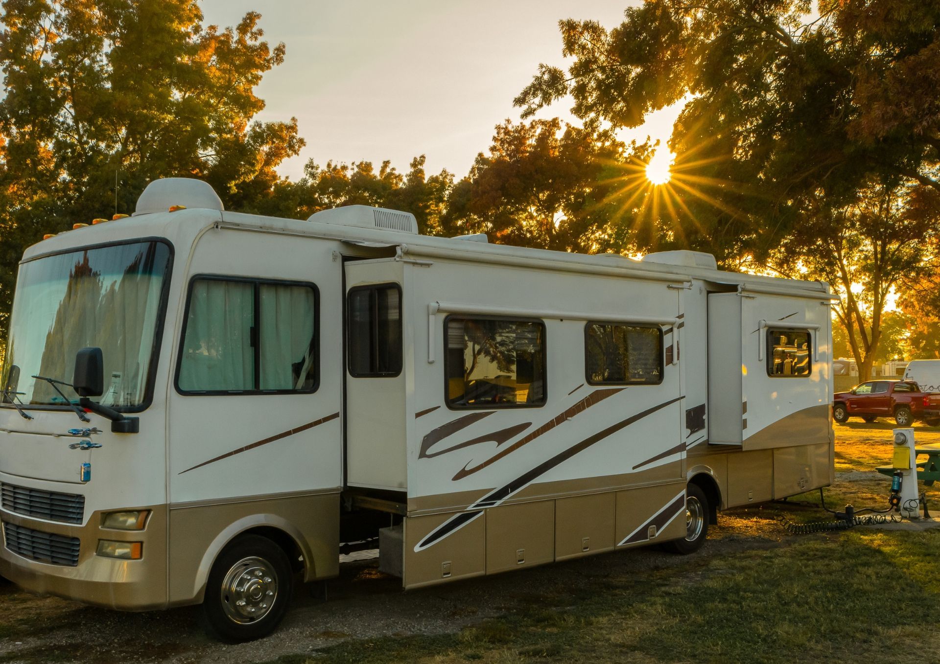 White motorhome parked in a wooded campsite at sunset, with sun shining through the trees
