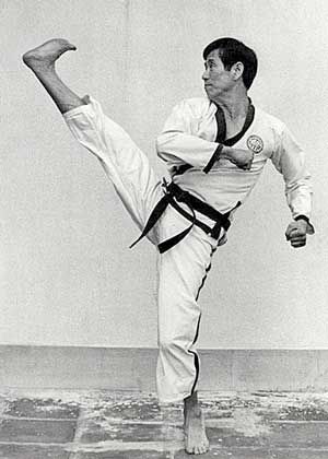 A man in a karate uniform is kicking his leg in a black and white photo.